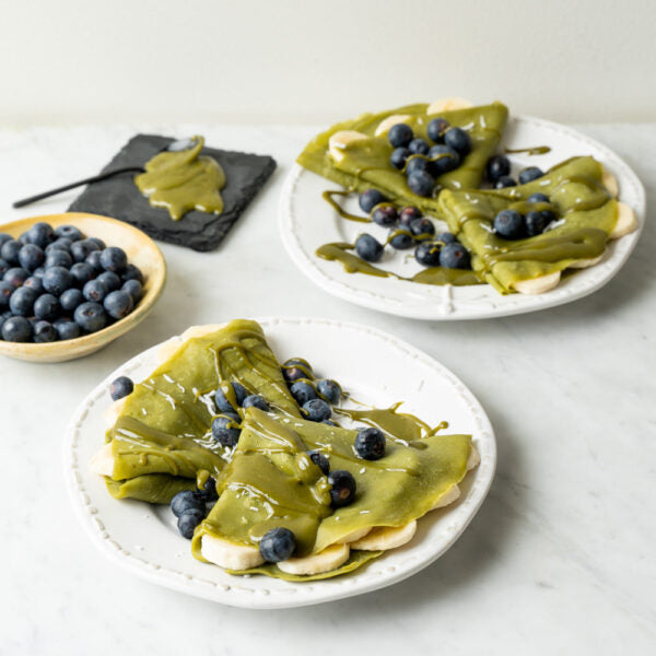 Stack of green matcha pancakes topped with fresh berries, next to a 1kg Matcha Maiden Organic Matcha Powder pouch.