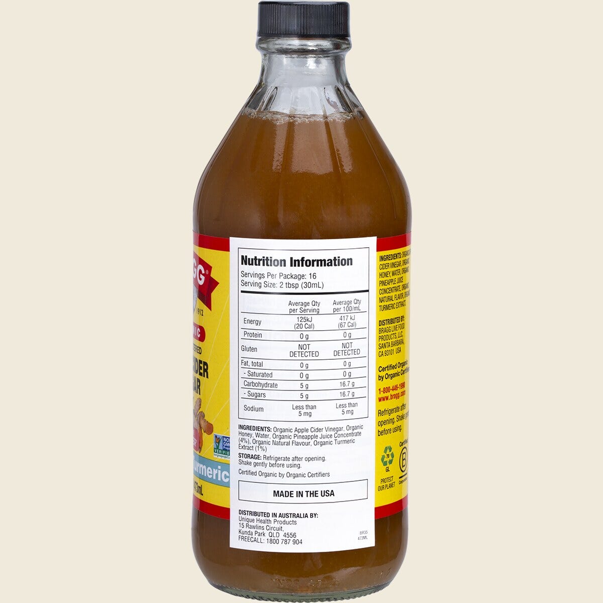 Right-angle view of a 473ml bottle of Bragg Pineapple Turmeric Apple Cider Vinegar Blend on a white background.