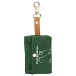 Green Biotuff compostable dog waste bag dispenser with a silver clip and a green bag roll on a white background.