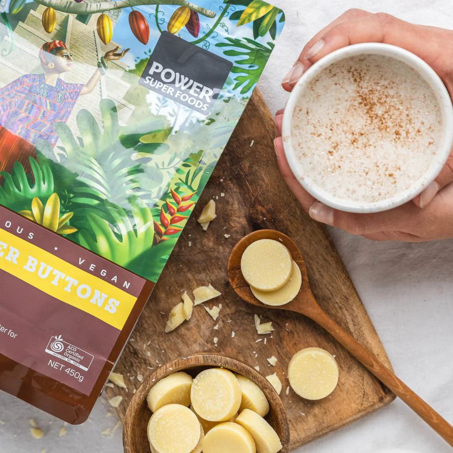 Organic raw cacao butter buttons in a wooden scoop on a white background.