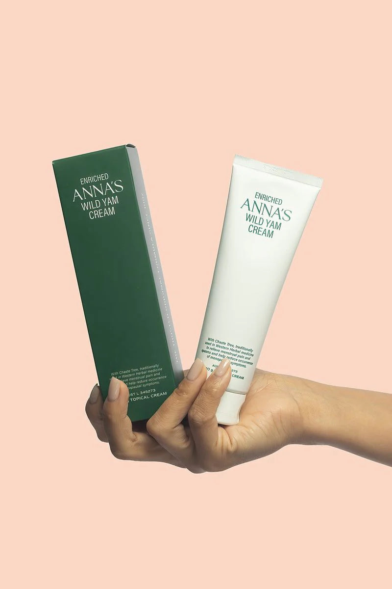 Close-up of a hand holding a white 100g jar of Anna's Wild Yam Cream for menstrual and menopausal relief.