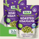 Two bags of DJ&A Roasted Edamame protein snack shown on a light beige background with a green branded card. The bags are predominantly purple and white with green edamame illustrations and a photo of roasted green edamame beans.