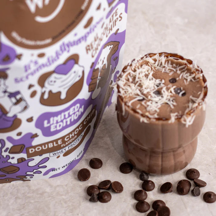 Scoop of Double Choc Chip Whey Protein Powder with dark chocolate chips and cocoa powder on a white background.