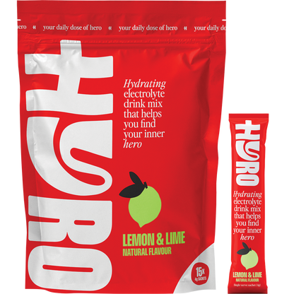 Hyro Lemon Lime Electrolyte box next to a prepared glass of citrus drink, a sachet, and fresh lemon and lime slices.