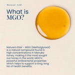 Lifestyle image of a Natural Life Manuka Honey MGO 800 jar next to a wooden honey dipper on a textured blue surface.