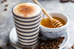 A cup of black coffee next to a jar of Australia's Manuka honey on a wooden surface with coffee beans.
