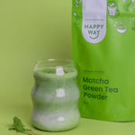 Wooden bowl of bright green matcha powder with a traditional bamboo whisk and spoon on a dark wooden surface.