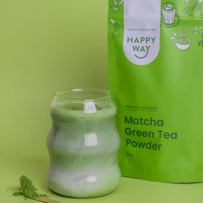 Wooden bowl of bright green matcha powder with a traditional bamboo whisk and spoon on a dark wooden surface.