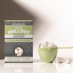 A bowl of white Organic Times Vanilla Mallows marshmallows with two mugs of hot chocolate on a wooden surface.