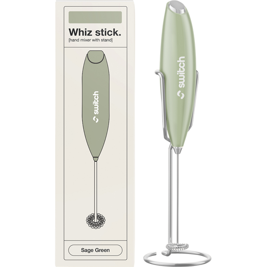 Sage green Switch Nutrition Whiz Stick electric handheld mixer with a silver whisk attachment and a matching storage stand.