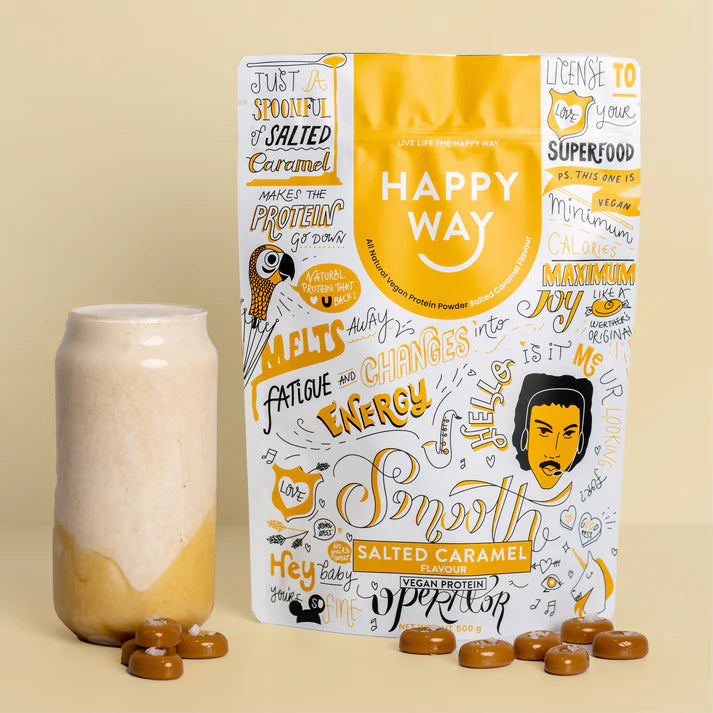A 500g bag of Happy Way Salted Caramel Vegan Protein Powder next to a glass of smoothie with a straw.