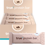 True Protein Cookies & Cream bar and display box on a white background with loose cookies and cream pieces.