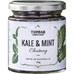 A jar of Turban Chopsticks Kale and Mint Chutney with fresh green ingredients on a white background.