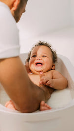 Close-up of a father gently washing his newborn baby's hair during a bath.