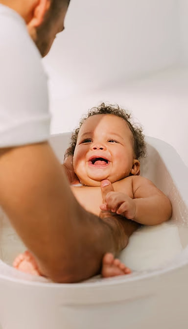 Close-up of a father gently washing his newborn baby's hair during a bath.