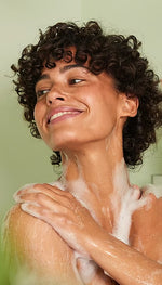 A person applying creamy white shower gel to their arm in a close-up lifestyle shot.