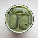 Vibrant green matcha powder being scooped from a white pouch with a traditional bamboo scoop.
