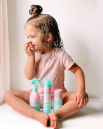 Child with curly hair smiling while holding a bottle of Giovanni Kids Curl Activator Spray.