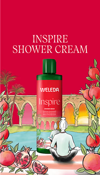 Weleda Inspire Pomegranate Shower Cream 400ml bottle with sliced pomegranates and flowers on a white background.