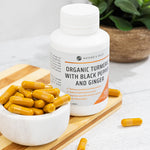 Close-up of three orange turmeric capsules with black pepper and ginger on a clean white background.